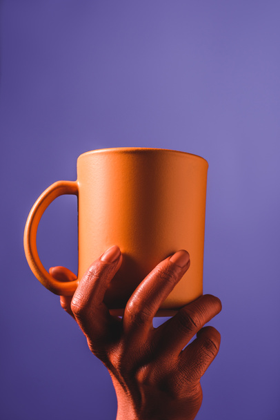 partial view of coral colored female hand with coral coffee cup on violet background,  color of 2019 concept - Fotografie, Obrázek