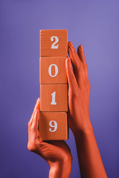 partial view of woman holding coral wooden cubes with 2019 numbers on blue background, color of 2019 concept - Fotó, kép