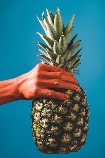 oříznutý pohled ženy držící ananas v korály barevné ruce na modrém pozadí, barva konceptu 2019 - Fotografie, Obrázek
