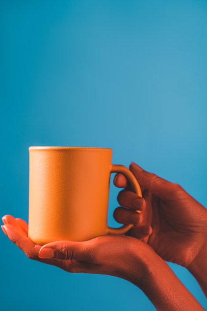 cropped view of woman holding coral coffee cup on blue background, color of 2019 concept - Fotografie, Obrázek