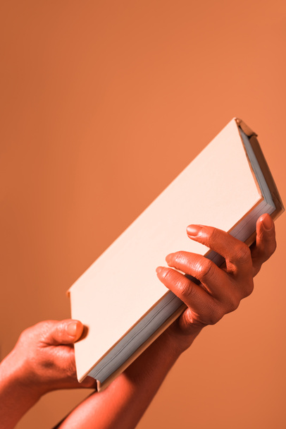 cropped view of woman holding book in coral colored hands on coral background, color of 2019 concept - Φωτογραφία, εικόνα