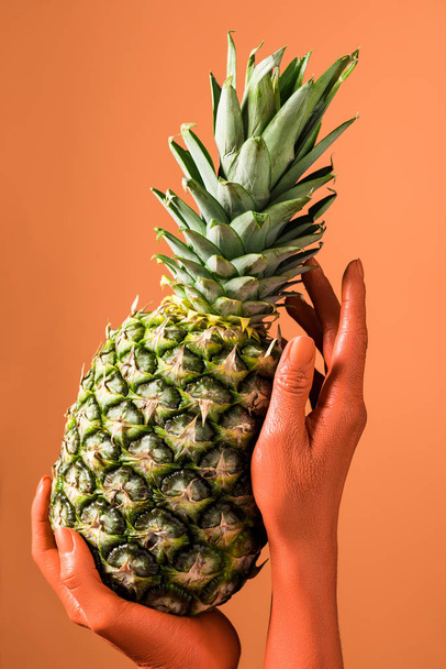 cropped view of coral colored female hands with pineapple on coral background, color of 2019 concept - Foto, afbeelding