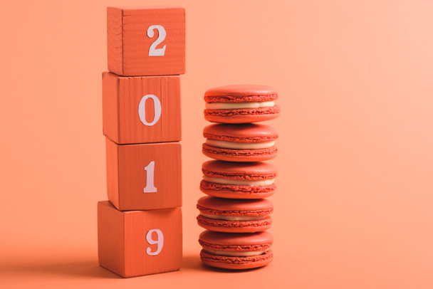stack of wooden cubes with 2019 numbers and macarons on coral background, color of 2019 concept - Φωτογραφία, εικόνα