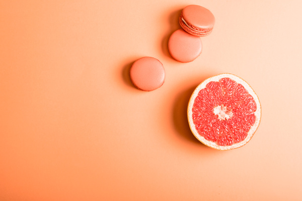 top view of coral macarons and grapefruit half on coral background, color of 2019 concept - Fotografie, Obrázek
