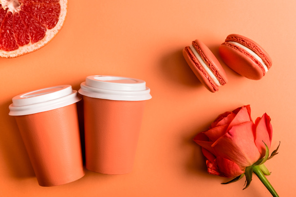 coral paper cups, rose flower, macarons and grapefruit half on coral background, color of 2019 concept - Φωτογραφία, εικόνα