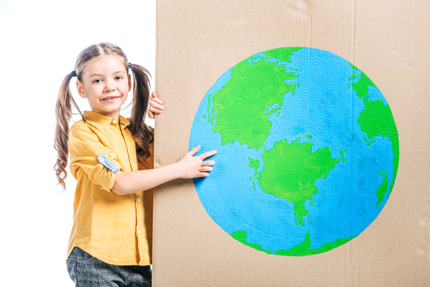 smiling kid pointing at globe sign on cardboard placard isolated on white, earth day concept - Photo, Image