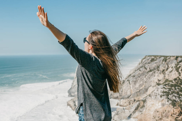 Девушка рядом с Атлантическим океаном в Португалии раздвигает руки по сторонам
 - Фото, изображение