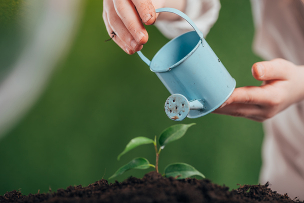 selective focus of child holding blue toy watering can and young green plant on blurred background, earth day concept - Photo, Image