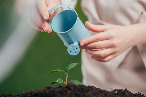 selective focus of kid holding blue toy watering can and young green plant on blurred background, earth day concept - Photo, Image