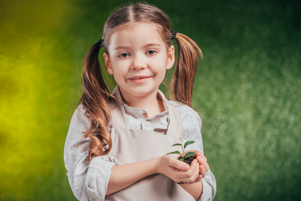 cute child holding young green plant on blurred background, earth day concept - Foto, afbeelding