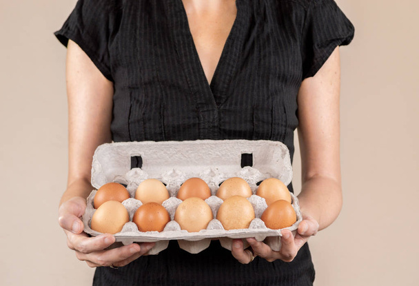 Mulher branca com camisa preta segurando uma caixa de ovo de papelão cheia de ovos de galinha
 - Foto, Imagem