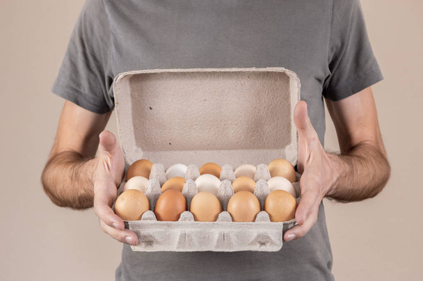 Kaukaski mężczyzna z szary tshirt trzymając jajko tekturowe pudełko pełne jaj kurzych. - Zdjęcie, obraz