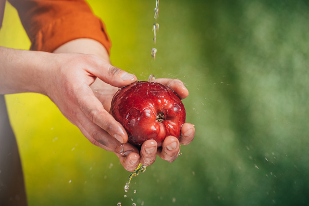 Selektywny fokus człowieka mycia apple pod nadmuchami wody na niewyraźne tło, koncepcja dzień ziemi - Zdjęcie, obraz