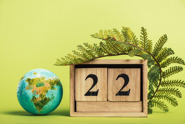 ξύλινο ημερολόγιο με την ημερομηνία «22 Απριλίου» και φύλλο πράσινο φτέρη σε ανοιχτό πράσινο φόντο - Φωτογραφία, εικόνα