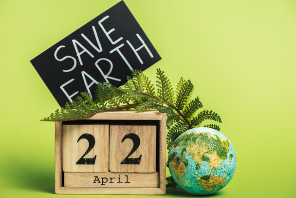 drewniane kalendarza z datą "22 kwietnia" i Paproć Zielony liść na jasnozielonym tłem - Zdjęcie, obraz