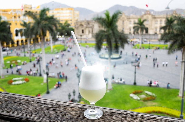 Pisco sour homemade cocktail with the background of the main square of Lima - Photo, Image