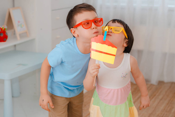 Мальчик и девочка играют со свечой с бумажным тортом. Детям, которые вместе кусают торт на свой день рождения
. - Фото, изображение