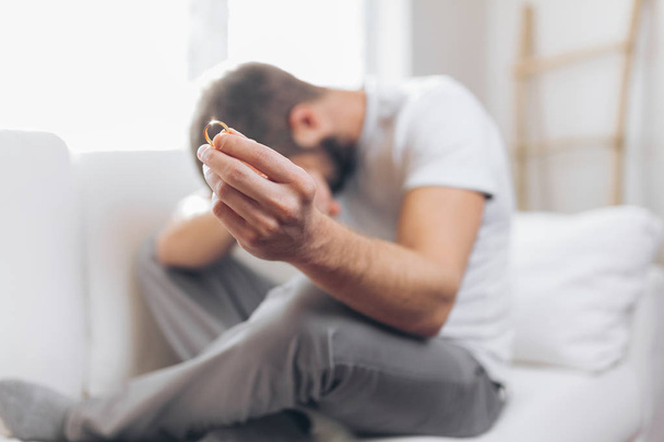 Heartbroken man at home holding a wedding ring - Photo, Image