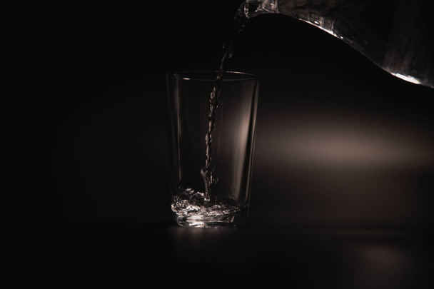 Water is poured into a transparent glass on a dark background - Fotoğraf, Görsel