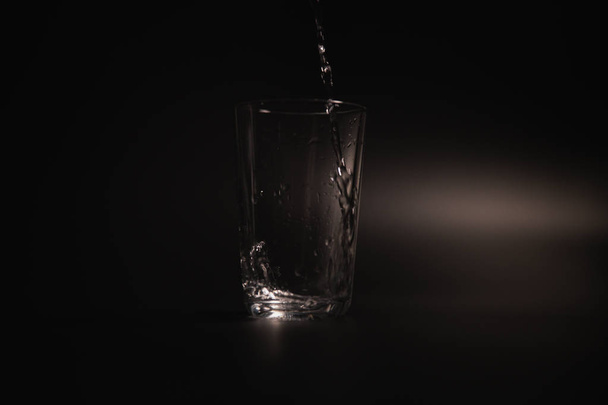 Water is poured into a transparent glass on a dark background - Фото, зображення