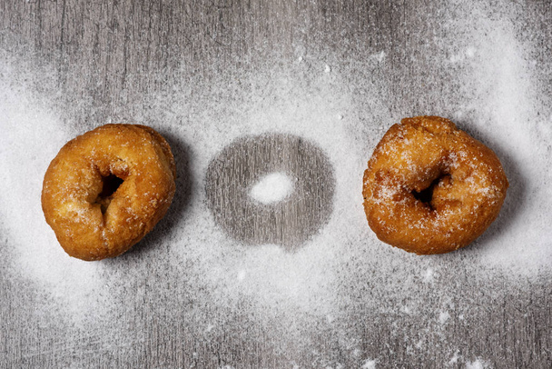 high angle view of some homemade rosquillas, spanish donuts typically eaten in Easter, on a rustic wooden table sprinkled with icing sugar - Photo, Image
