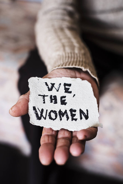 closeup of an old caucasian woman indoors with a piece of paper in her hand with the text we the women written in it - Photo, Image