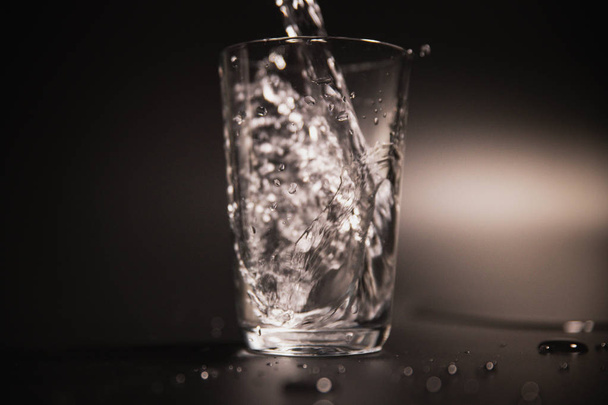 Вода наливается в прозрачное стекло на темном фоне
 - Фото, изображение