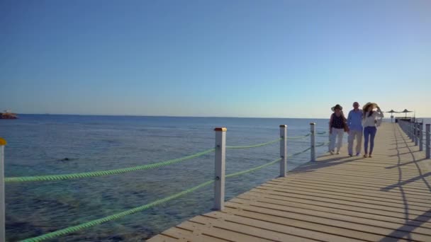 Senior paar wandelen met hun volwassen dochter op pier door de rode zee. Familie genieten van de zomervakantie. - Video