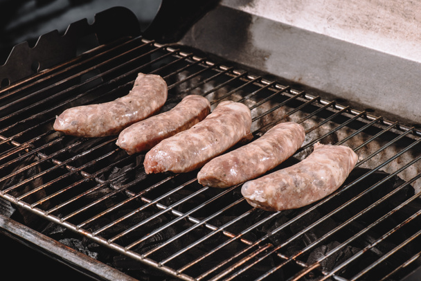 raw pork sausages cooking on barbecue grill grates  - 写真・画像