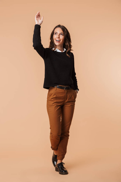 Full length of a cheerful young woman wearing sweater standing isolated over beige background, looking away - Fotoğraf, Görsel
