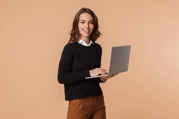 Фото 20-летней женщины, стоящей и держащей ноутбук на бежевом фоне
 - Фото, изображение