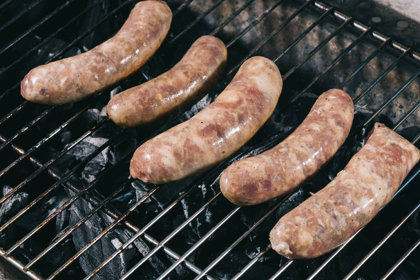 сырые свежие колбасы, готовящиеся на решетке гриля для барбекю
 - Фото, изображение