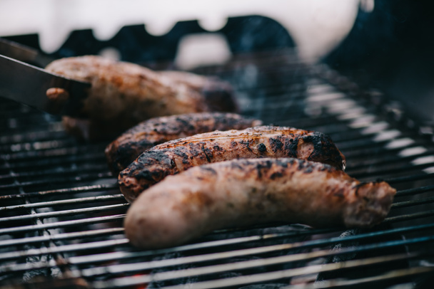 selective focus of grilled meat sausages and tweezers on barbecue grid - Foto, Imagem