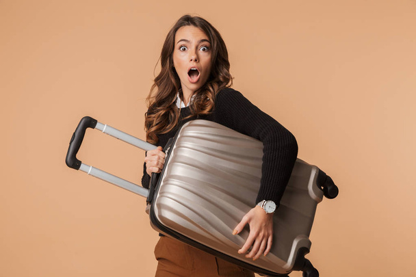 Зображення веселої жінки 20-х років, що ходить і несе багаж ізольовано на бежевому тлі
 - Фото, зображення