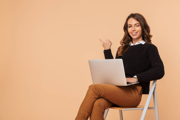 Image of a beautiful amazing young woman posing isolated sitting on stool using laptop computer pointing. - Фото, зображення
