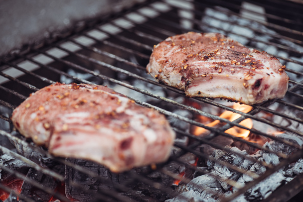 selective focus of juicy raw steaks grilling on barbecue grid - Fotó, kép