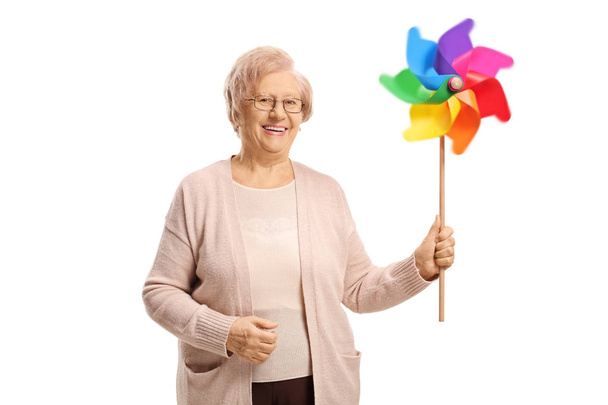 Smiling elderly woman holding a spinning pinwheel isolated on white background - Foto, afbeelding