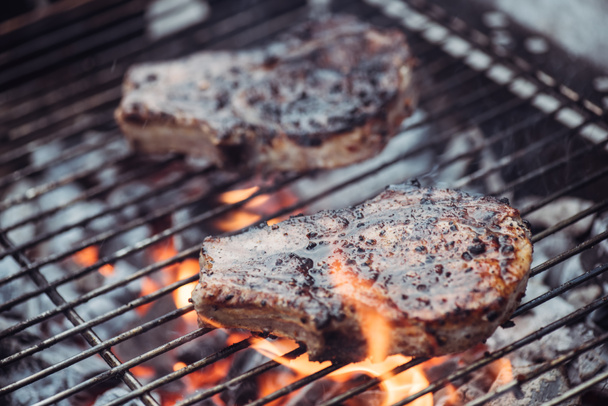 selective focus of juicy tasty steaks grilling on barbecue grid with smoke - Photo, Image