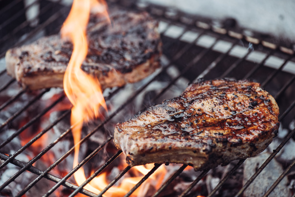fuoco selettivo di succose gustose bistecche grigliate su barbecue grado con fiamma
  - Foto, immagini