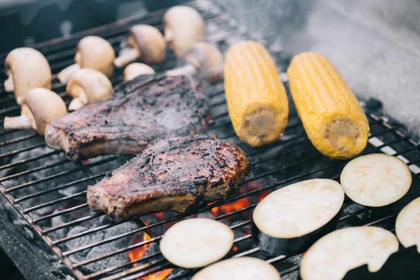 selective focus of juicy tasty steaks grilling on bbq grid with mushrooms, corn and sliced eggplant - Foto, Imagem