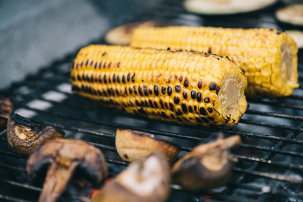 selective focus of yellow corn with crust and mushrooms grilling on barbecue grid - Photo, Image