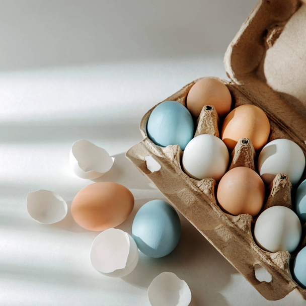 Натурально окрашенные коричневые и белые яйца в яичной коробке с солнечными лучами. Пасхальная концепция
.   - Фото, изображение