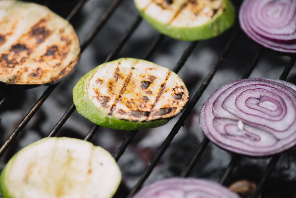 selective focus of onion and zucchini slices grilling on barbecue grid - Фото, зображення