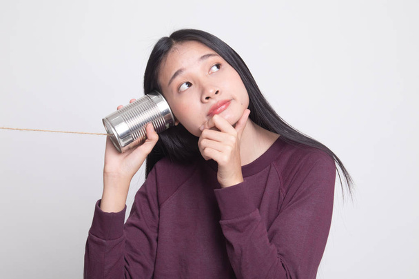 Young Asian woman hearing with tin can phone and thinking on white background - Foto, Bild