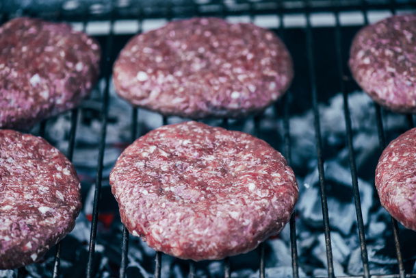 close up of uncooked fresh burger cutlets grilling on bbq grid - Фото, зображення