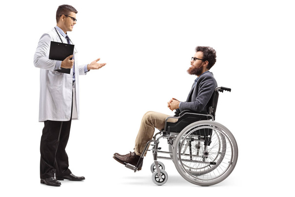 Full length profile shot of a young male doctor talking to a bearded man in a wheelchair isolated on white background - Fotografie, Obrázek