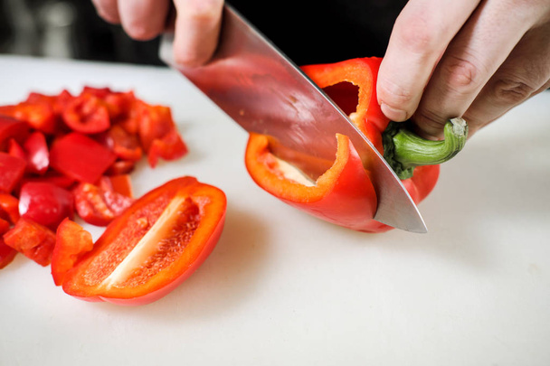 Мужчина-повар режет овощи для салата в ресторане в черном фартуке. Белая разделочная доска, крупный план рук
. - Фото, изображение