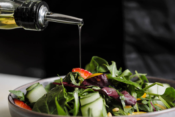 Кулинарный салат шеф-повар на кухне ресторана. Полив оливкового масла из бутылки дозатором
. - Фото, изображение
