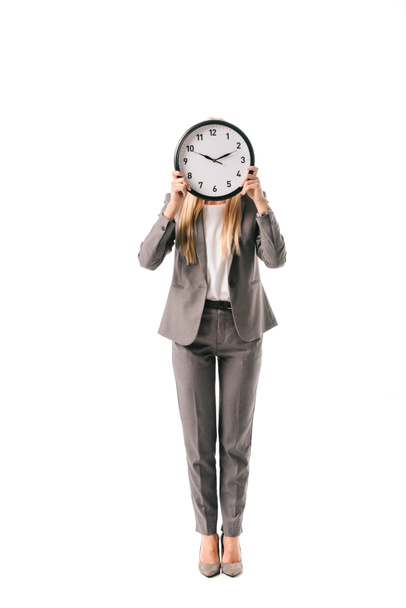 businesswoman in suit holding clock in front of the face, isolated on white - Фото, зображення