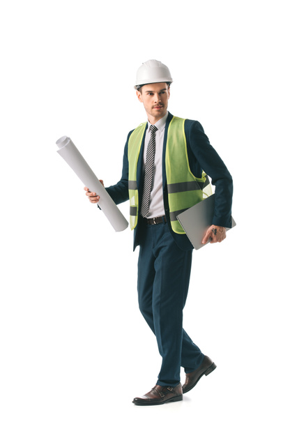 male architect in hardhat and safety vest walking with blueprint and laptop, isolated on white - Foto, Bild